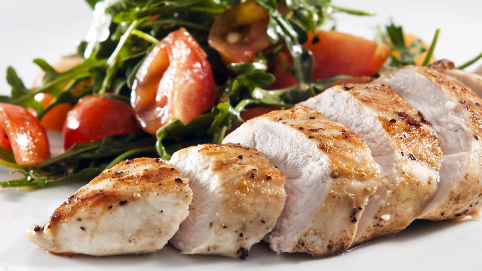 green salad with tomatoes alongside sliced pork loin on a white serving plate