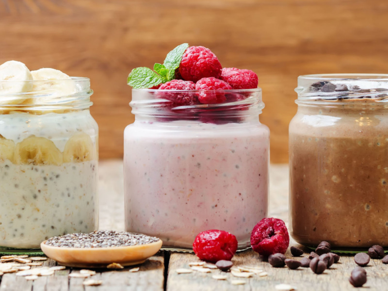 Three jars of yogurt on a table surrounded by various fruit and nuts