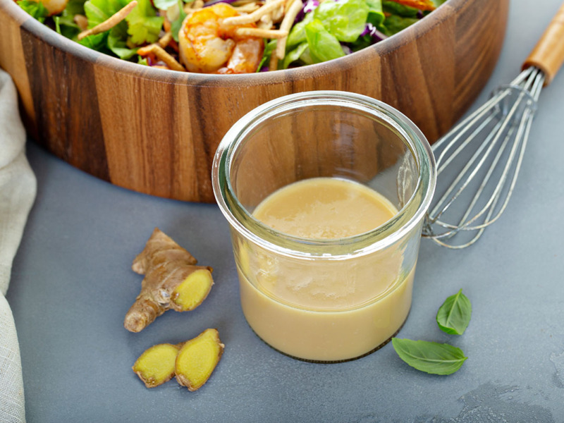 bowl of salad with a jar of dressing along with ginger and basil leafs