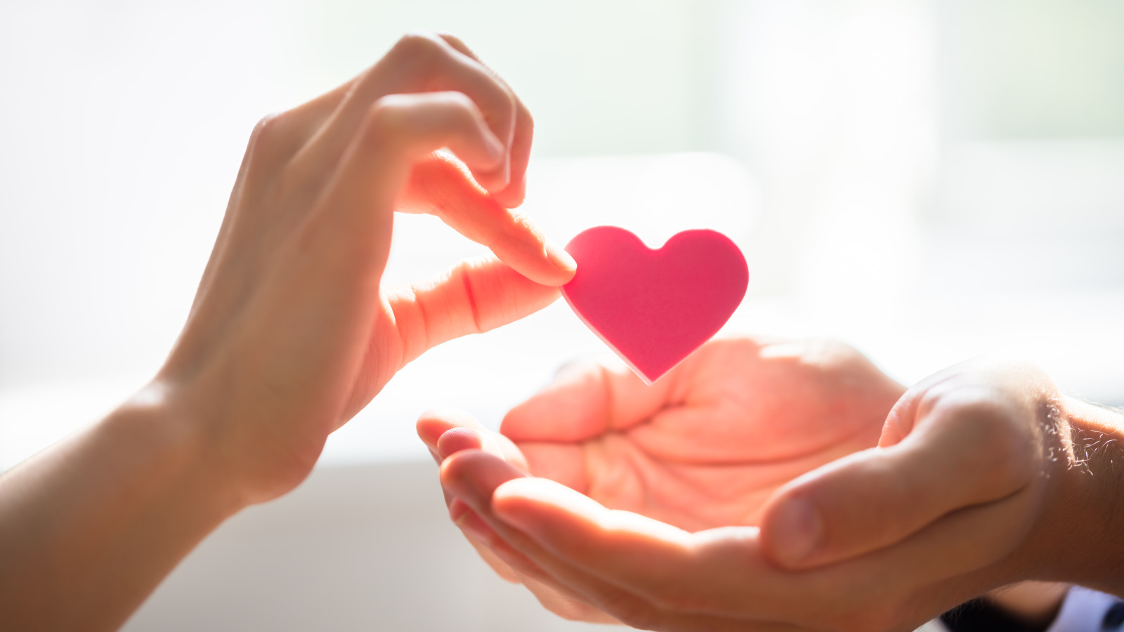 close up of a women's hand, passing a paper cutout heart to a man's open palm