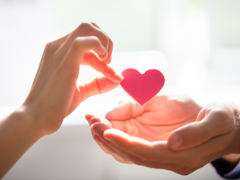 close up of a women's hand, passing a paper cutout heart to a man's open palm