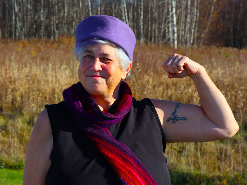 Patient standing in a field flexing her left arm to show strength after rehabilitation