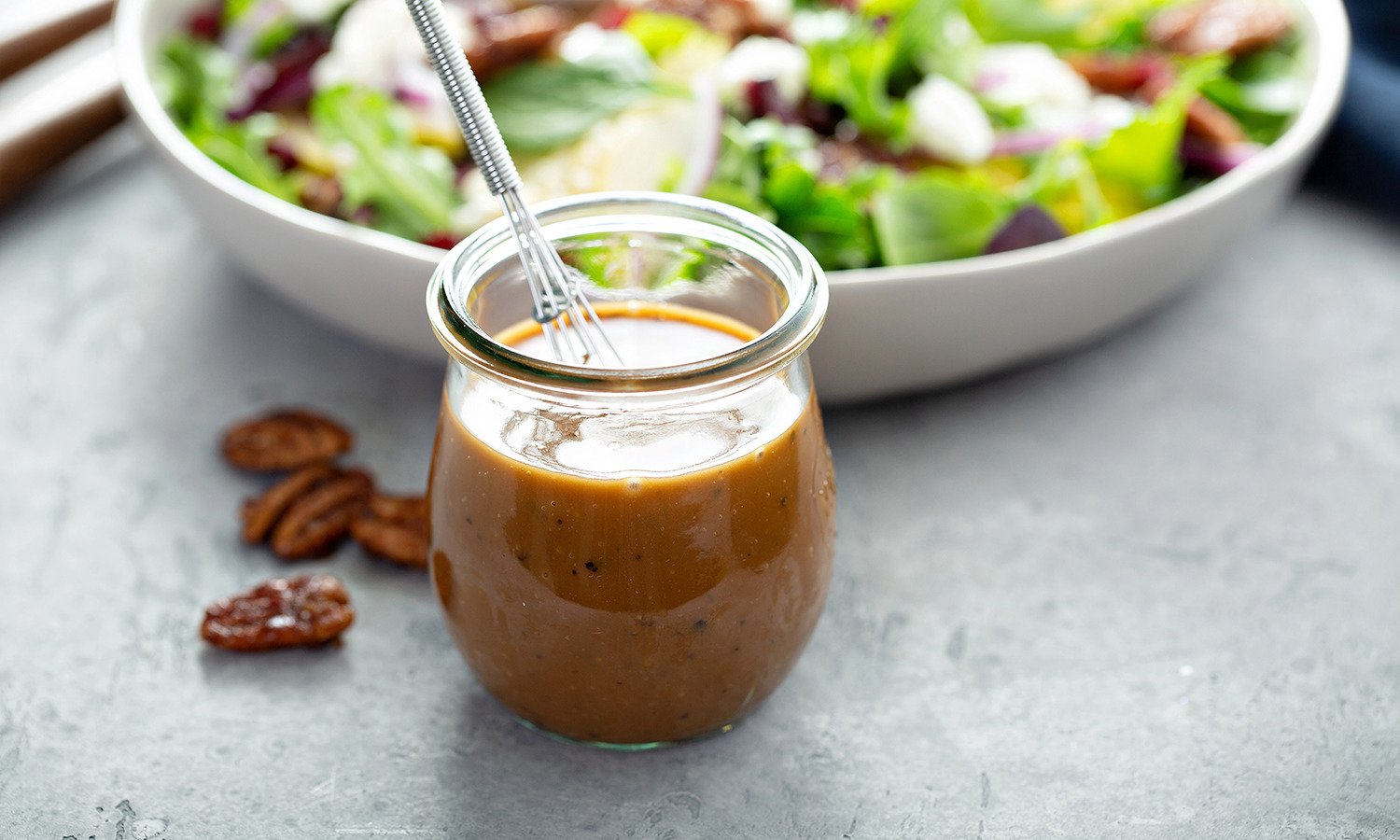 Jar of salad dressing in front of a white bowl filled with a green salad