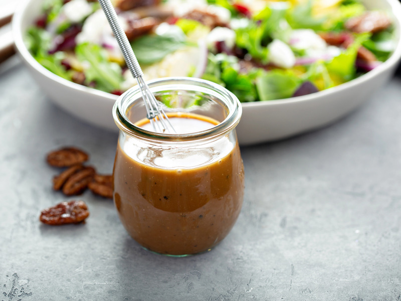 Jar of salad dressing in front of a white bowl filled with a green salad