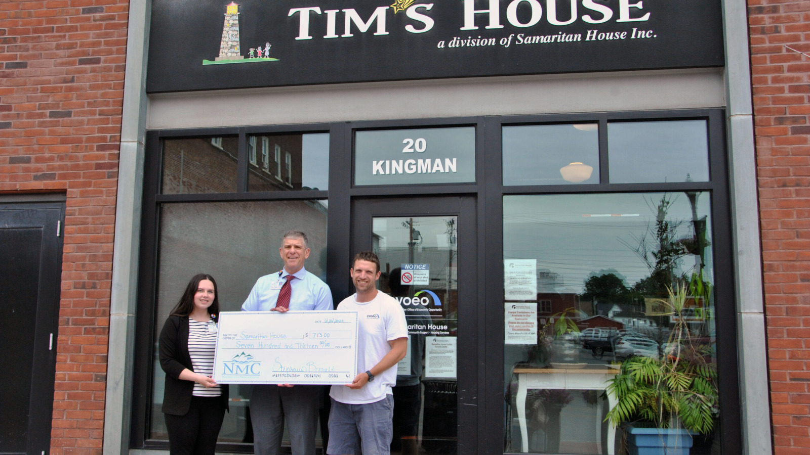 Peter Wright, CEO of Northwestern Medical Center, handing a ceremonial check to representatives of Tim's House, while standing in front of Tim's house at 20 Kingman St. St. Albans vermont