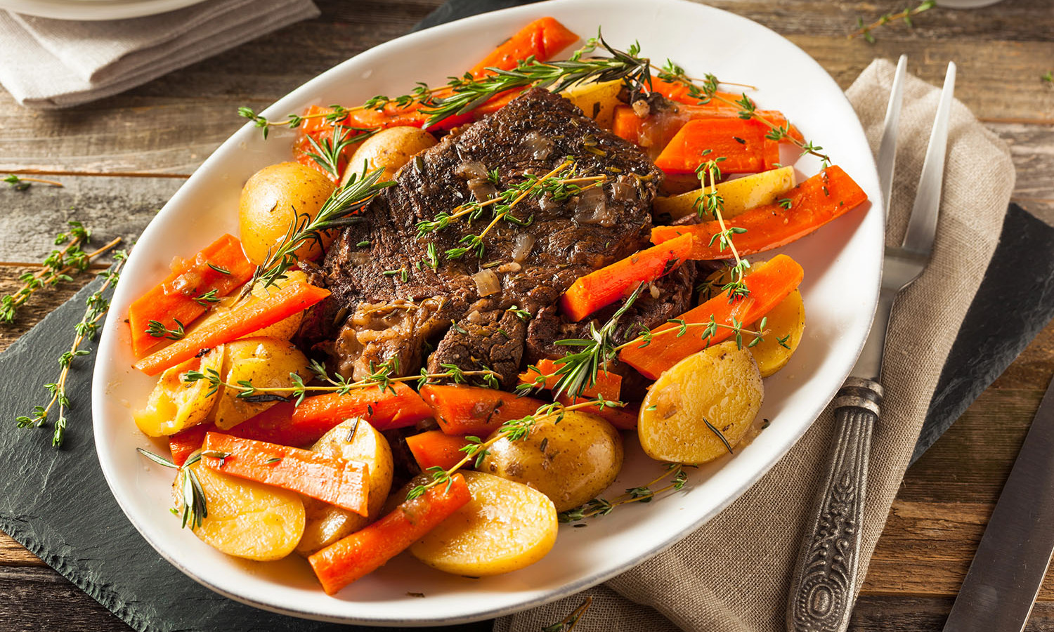Pot roast surrounded by potatoes and carrots on a white server platter