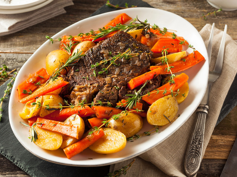 Pot roast surrounded by potatoes and carrots on a white server platter
