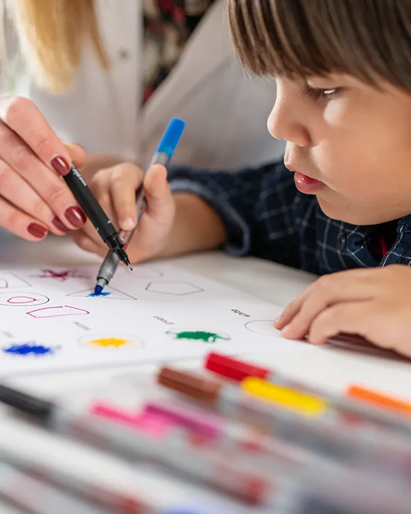 Young boy around 4yrs old drawing with the assistance of pediatric development team